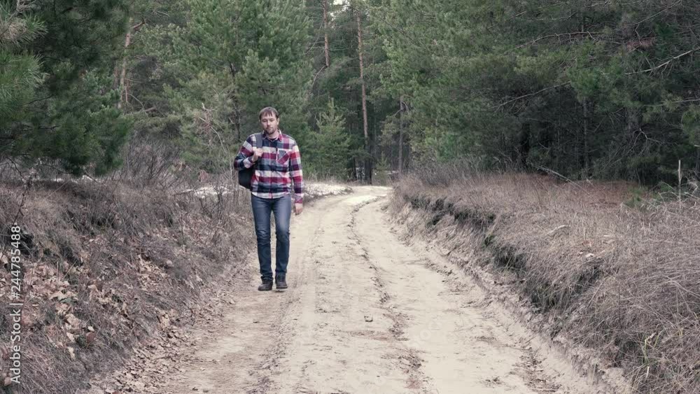 Adult male in casual outfit walking on dirty countryside road and looking around while travelling in nature Adult male in casual outfit walking on dirty countryside road and looking around while travelling in nature