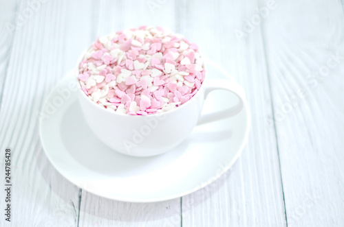 White coffee cup on wooden floor.Many small hearts, white and pink, are in a cup of coffee.Pink square wood with 1 and 4 white numbers, white glass..