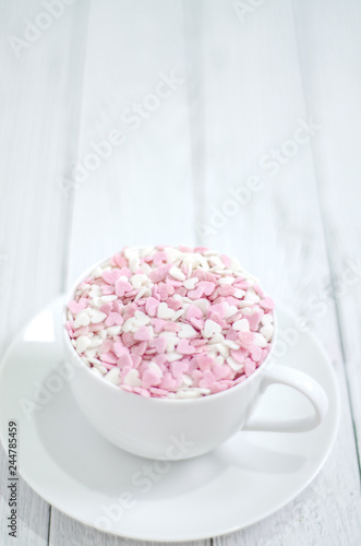 White coffee cup on wooden floor.Many small hearts, white and pink, are in a cup of coffee.Pink square wood with 1 and 4 white numbers, white glass..