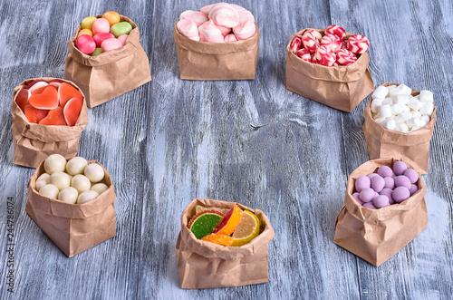 Colored candy in paper bags on wooden background