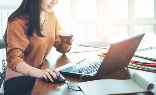 Close up business woman using computer for working in office with coffee on wooden table. Selective focus blur background