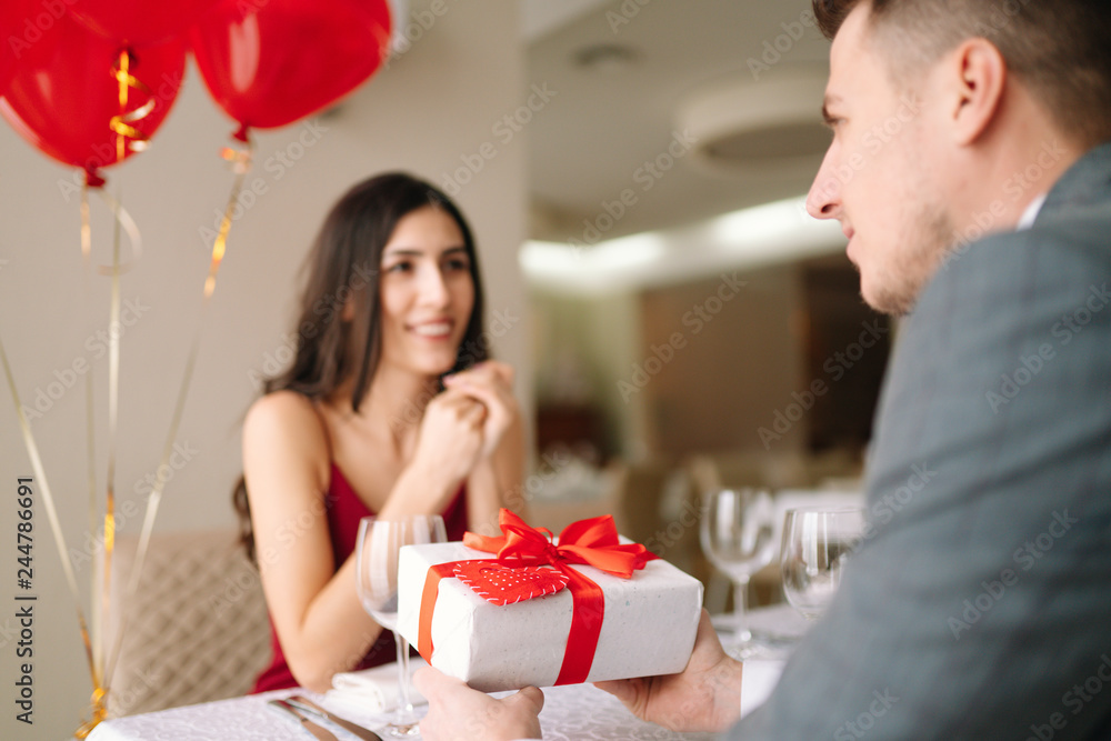 Valentine's Day concept. Happy couple in love with. A young loving couple celebrating Valentine's Day in the restaurant. Lovers give each other gifts. Romance restaurant for Valentine's Day- concept. Valentine's Day concept. Happy couple in love with. A young loving couple celebrating Valentine's Day in the restaurant. Lovers give each other gifts. Romance restaurant for Valentine's Day- concept.