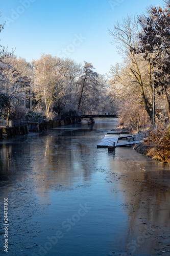 Ansicht vom teilweise gefrorenen Fluss "Weisse Elster"mit Baeumen und einem Wehr bei blauen Himmel