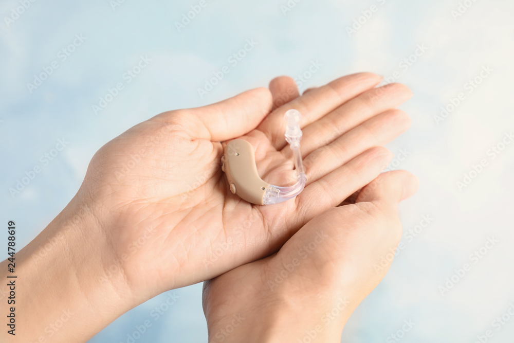 Woman holding hearing aid on color background, closeup
