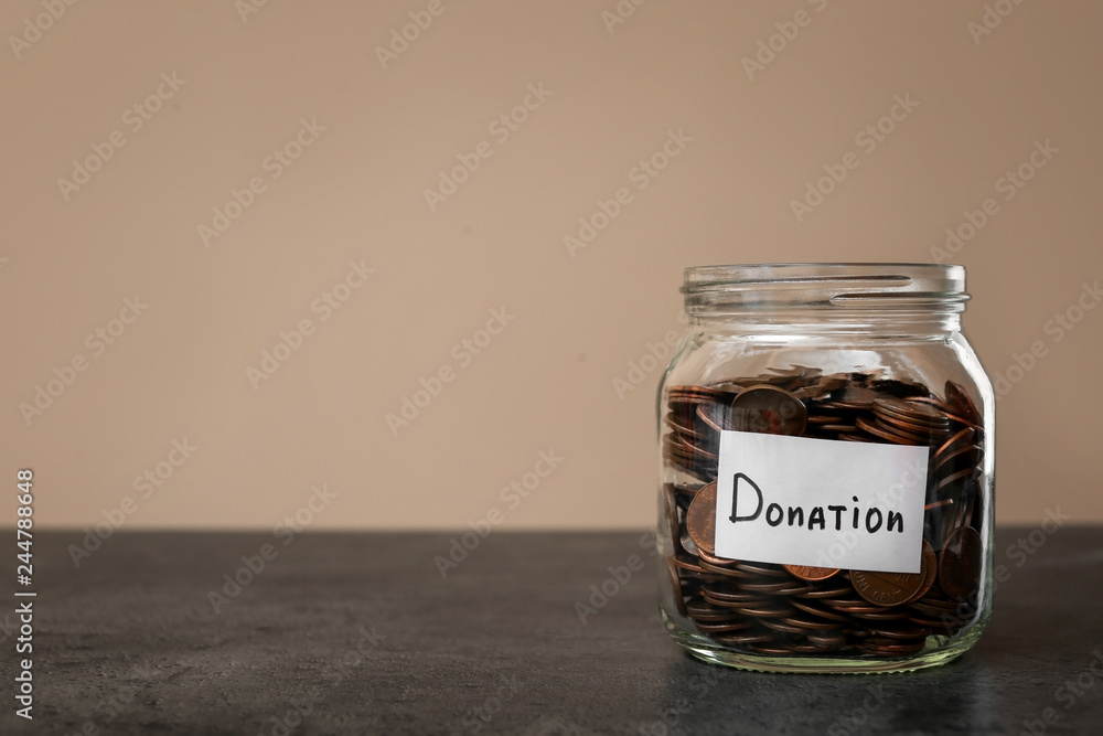 Donation jar with coins on table against color background. Space for text Donation jar with coins on table against color background. Space for text