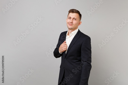 Portrait of successful young business man in classic black suit and white shirt standing isolated on grey wall background in studio. Achievement career wealth business concept. Mock up copy space.