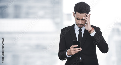 Depressed businessman looking at his smartphone with bad news about his financeial crisis photo