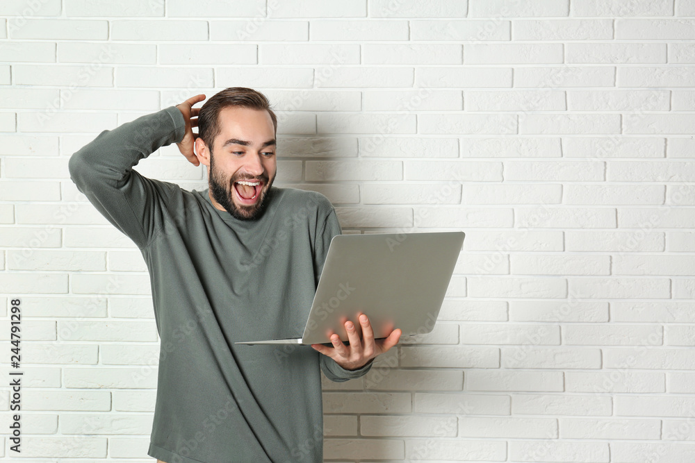 Emotional young man with laptop celebrating victory near brick wall. Space for text Emotional young man with laptop celebrating victory near brick wall. Space for text