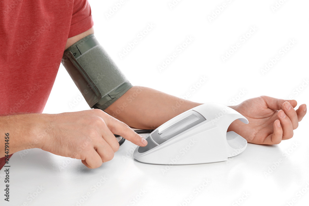 Fototapeta premium Man checking blood pressure with sphygmomanometer at table against white background, closeup. Cardiology concept