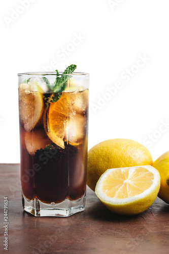 Cuba Libre cocktail with rum, cola, mint, lemon and ice in the glass on a brown table and white background