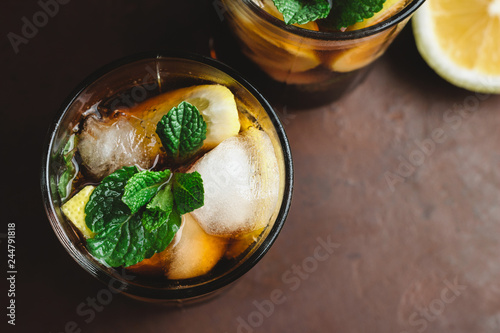 Photography Cuba Libre cocktail with rum, cola, mint, lemon and ice in the glass on a brown