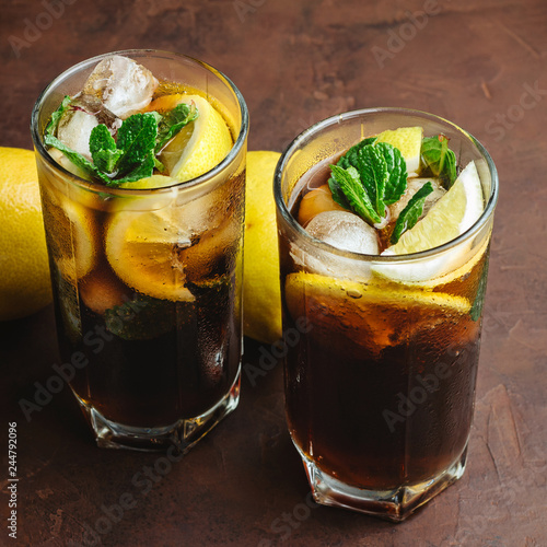 Cuba Libre cocktail with rum, cola, mint, lemon and ice in the glass on a brown background