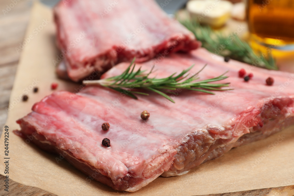Raw ribs with pepper and rosemary on parchment, closeup. Fresh meat