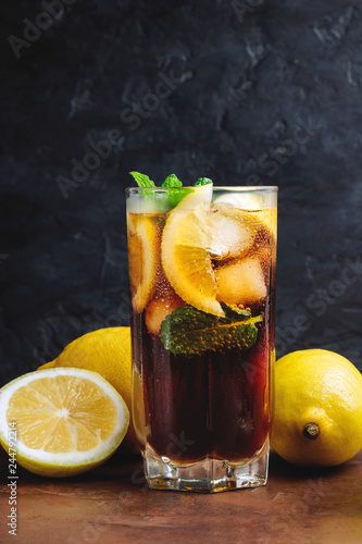Cuba Libre cocktail with rum, cola, mint, lemon and ice in the glass on a brown table and black background