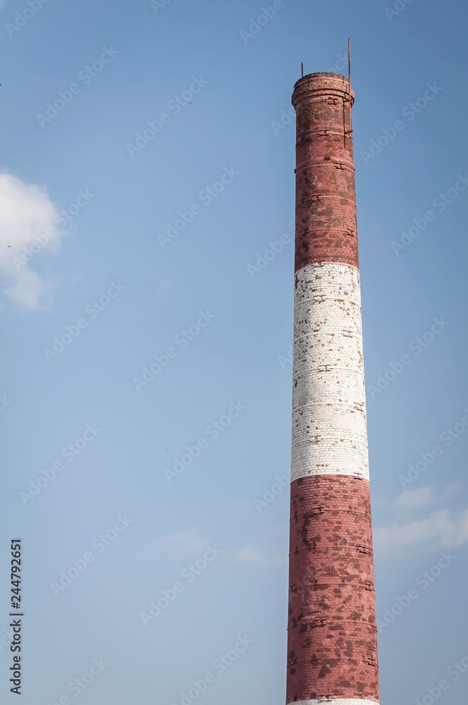 Red and white old brick industrial pipe against the blue sky. Old industry concept image. Desolated old factory, ecology, industrial renewal, globalization.