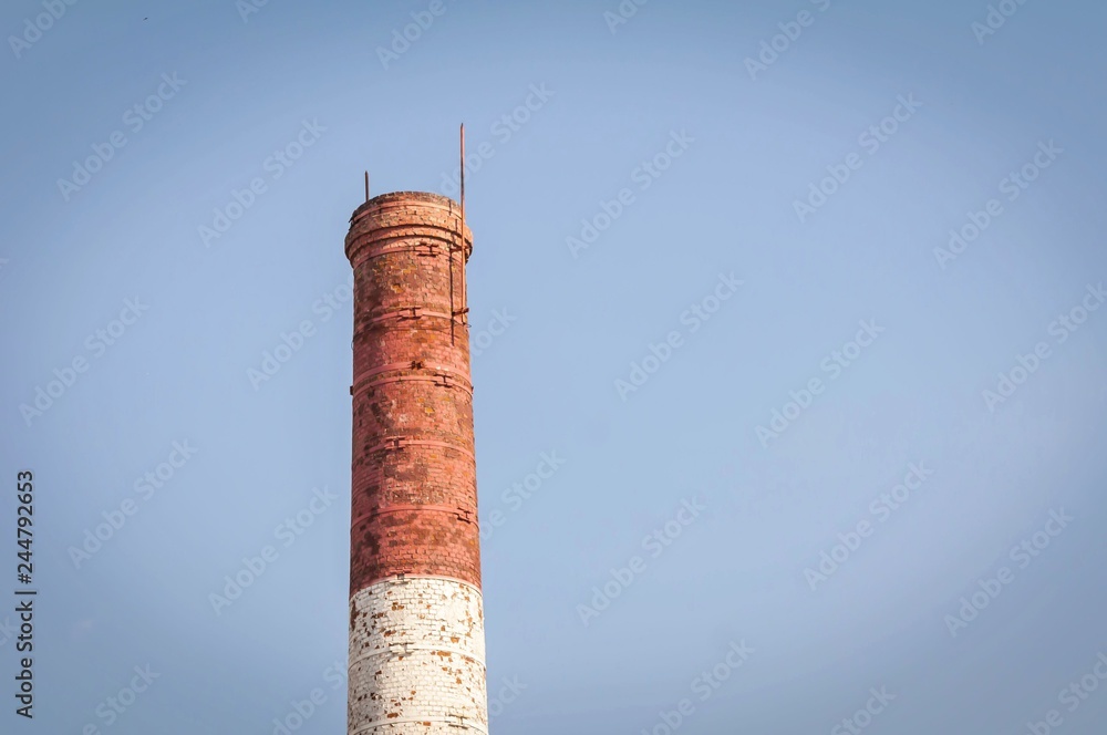 Red and white old brick industrial pipe against the blue sky. Old industry concept image. Desolated old factory, ecology, industrial renewal, globalization.