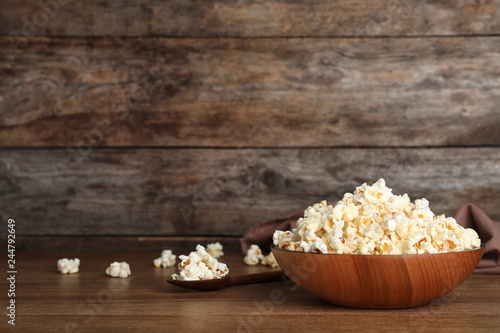 Wooden bowl with tasty popcorn on table. Space for text