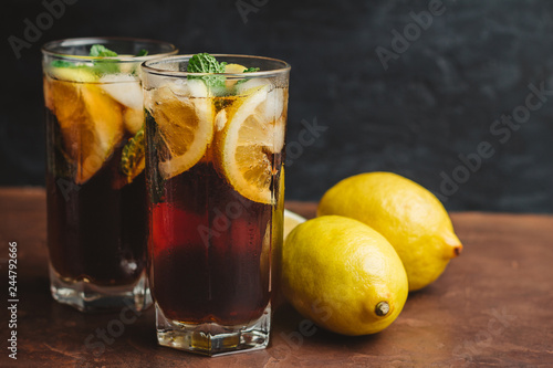Cuba Libre cocktail with rum, cola, mint, lemon and ice in the glass on a brown table and black background