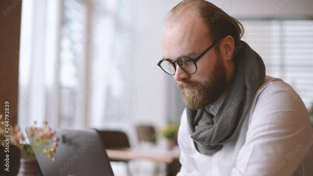 Bearded man in casual sitting in cafe and using laptop Bearded man in casual sitting in cafe and using laptop