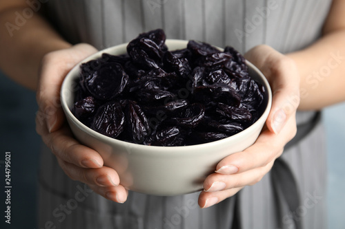 Woman holding bowl of dried plums, closeup. Healthy fruit