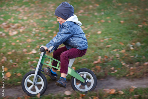 Fototapeta Naklejka Na Ścianę i Meble -  A small child rides a racer in an autumn park.