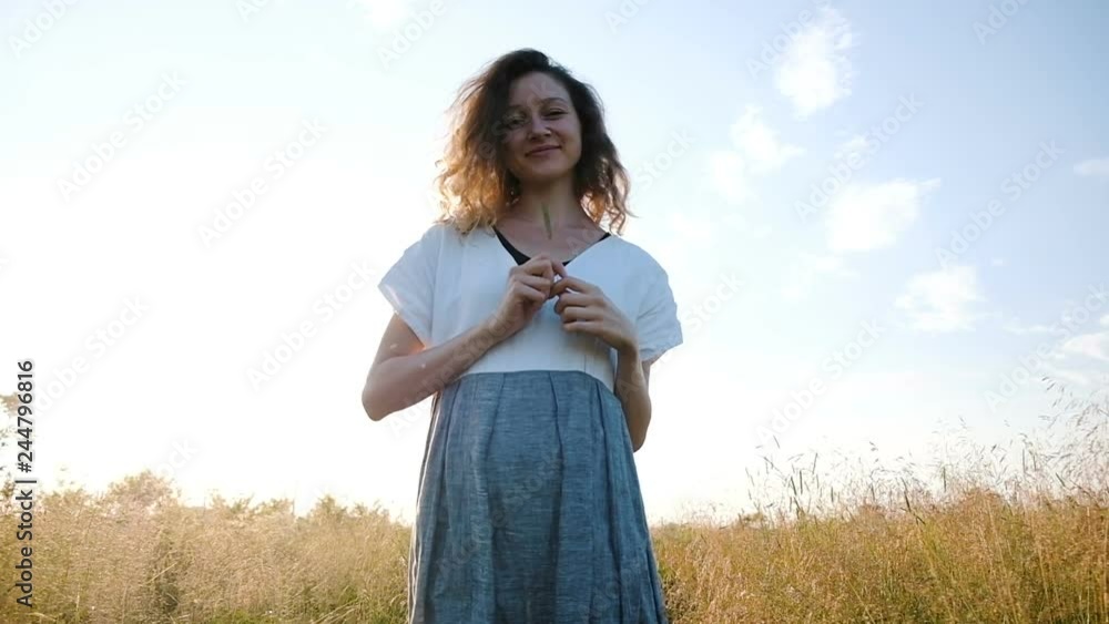 Woman in a dress with a grass in her hand walks in a field at sunset, slow motion and camera movement Woman in a dress with a grass in her hand walks in a field at sunset, slow motion and camera movement