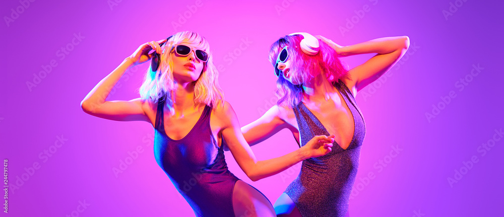 Fashion. Two sexy DJ girl in Colorful neon light having fun dance, friends. Glamour party fitness woman with Dyed Hair. Young beautiful model enjoy nightlife. Creative art banner