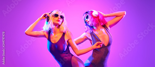 Fashion. Two sexy DJ girl in Colorful neon light having fun dance, friends. Glamour party fitness woman with Dyed Hair. Young beautiful model enjoy nightlife. Creative art banner