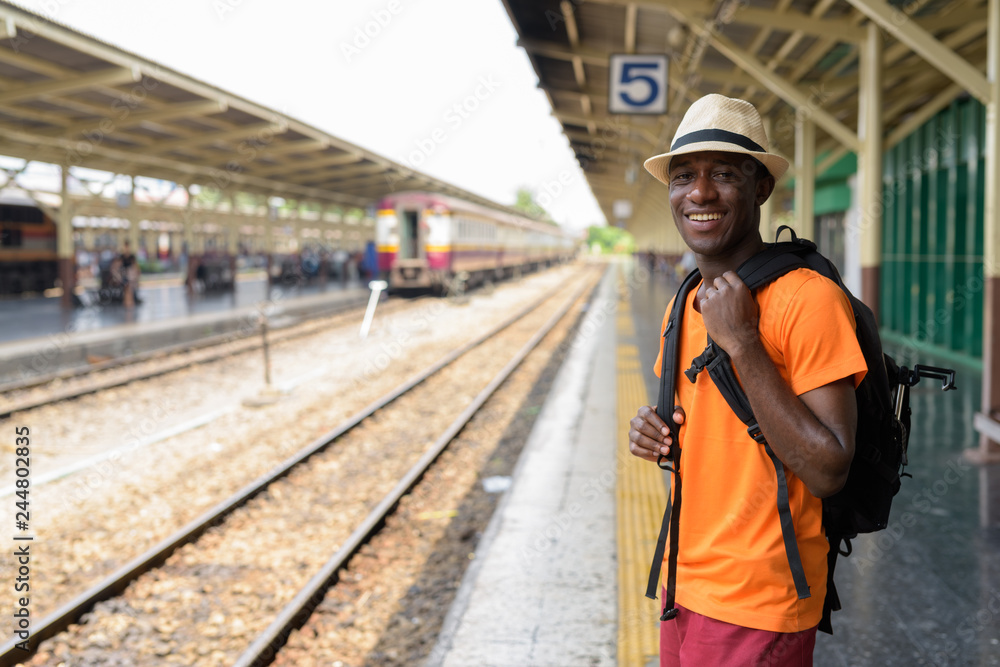 Happy young African tourist man smiling while waiting for train Happy young African tourist man smiling while waiting for train