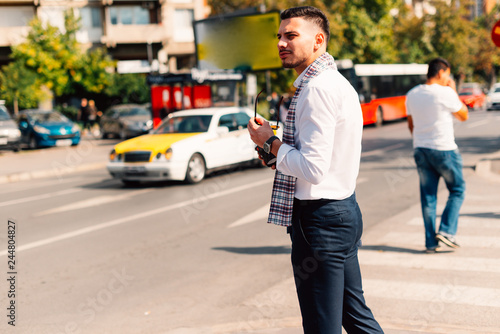 A modern businessman is looking curious in the city while crossing the pedestrian with coffee and mobile in his hands. © qunica.com