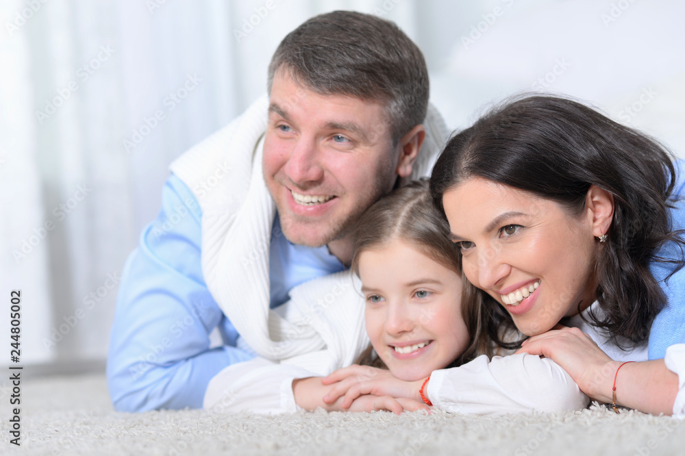 Happy parents and daughter lying on floor in room