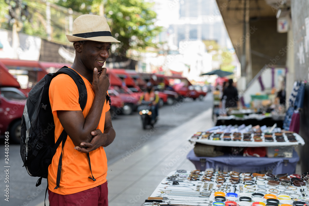 Young happy black African tourist man smiling and shopping outdoors Young happy black African tourist man smiling and shopping outdoors