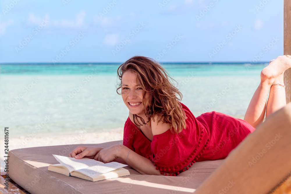 woman on a sunchair reading a book in a tropical location. Clear turquoise water as background