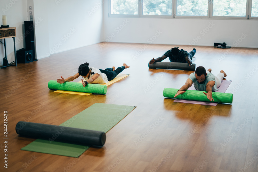 Naklejka premium People doing exercises with foam rollers in the gym