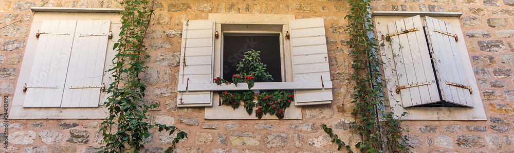Windows with shutters and pots with flowers in the stone wall