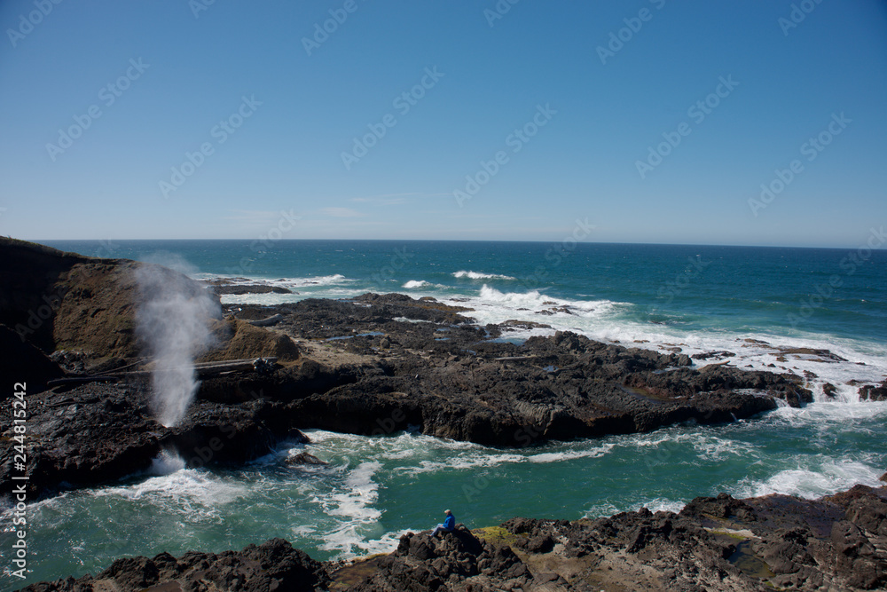 The Spouting Horn at Cape Perpetua on the Oregon Coast. A man watching the feature across a inlet of water. The Spouting Horn at Cape Perpetua on the Oregon Coast. A man watching the feature across a inlet of water.