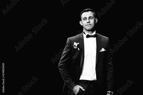 the fiance in an elegant suit holds his hand in his pocket on a black and white photography