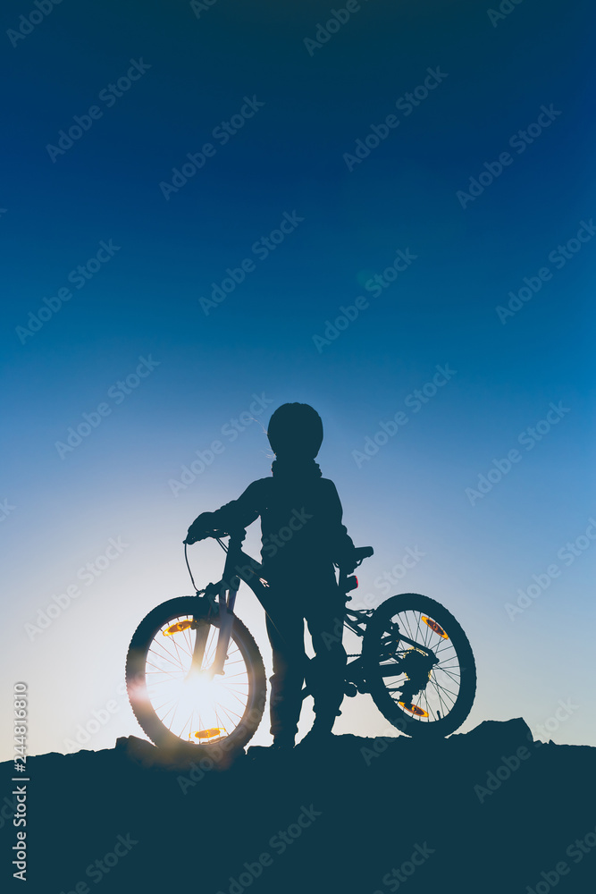 Fototapeta premium Silhouette of a little girl with a bicycle at sunset