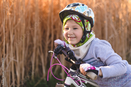 Cute little girl with a bicycle in the autumn on the background of reeds