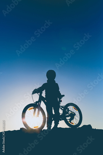 Silhouette of a little girl with a bicycle at sunset