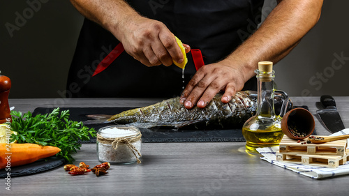 Add lemon juice to fish carp in chef hands, black background. Food recipe photo, copy text
