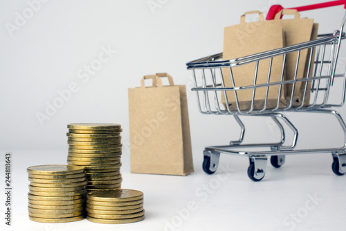 cheap and inexpensive online shopping. shopping bags in metal wire shopping cart stacks of coins, white background