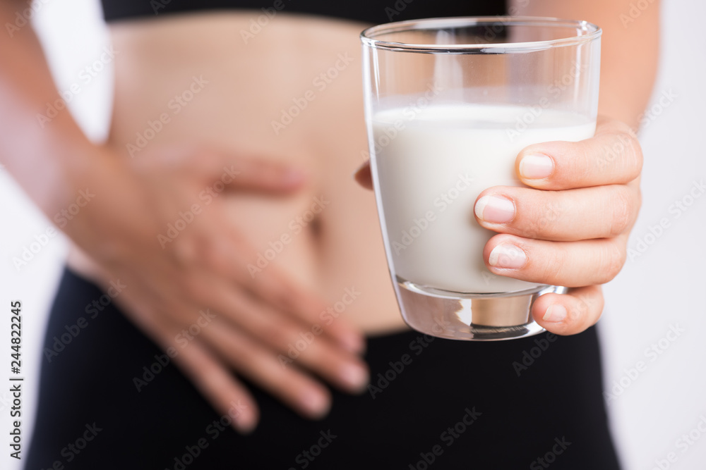Woman hand holding glass of milk having bad stomach ache because of Lactose intolerance. health problem with dairy food products, Healthcare and medical concept. Woman hand holding glass of milk having bad stomach ache because of Lactose intolerance. health problem with dairy food products, Healthcare and medical concept.