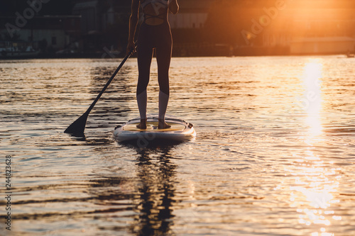 SUP silhouette of young girl paddle boarding at sunset