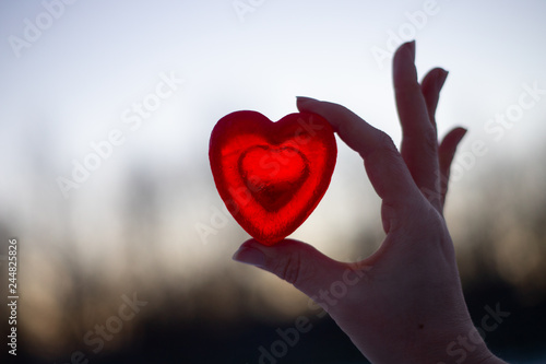The girl holds with one hand a heart symbol from glycerin of red heart in the street in a clear frosty weather