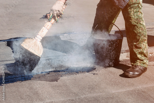 Worker repairs the roof with molten tar from a bucket with a broom.