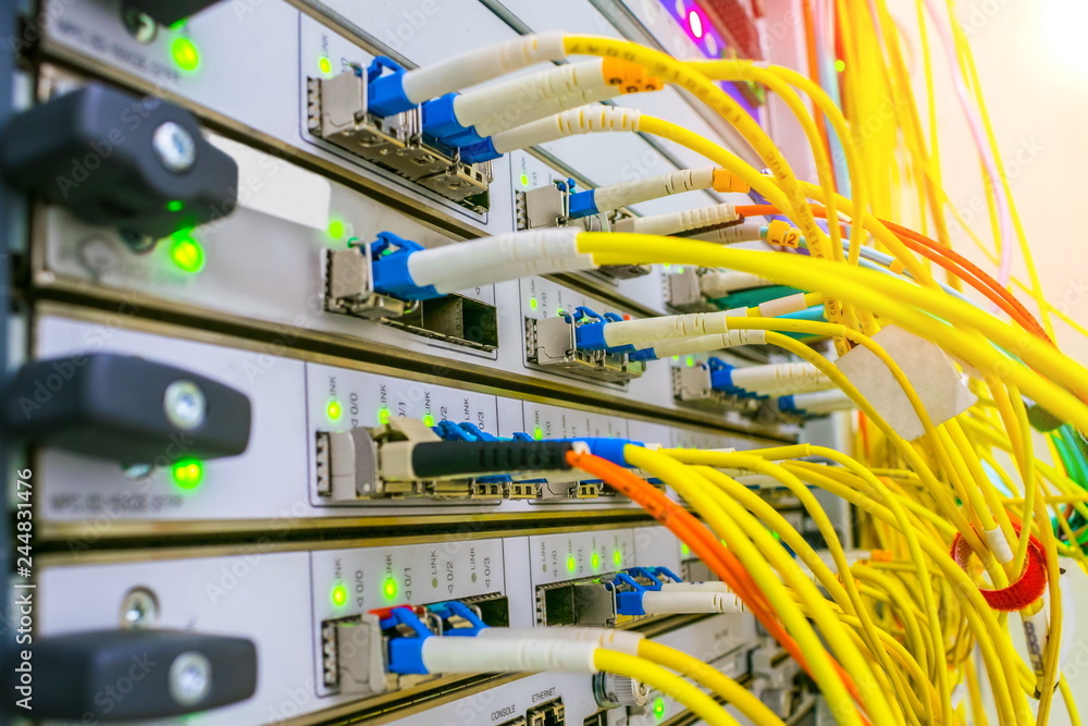 Powerful server equipment datacenter. Yellow fiber optic telecommunications cables are connected to the router of the Internet provider. An external gateway running on the Border Gateway Protocol.