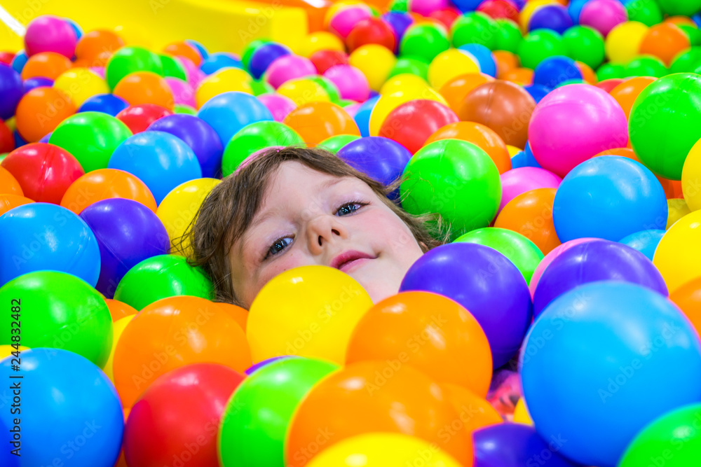 A little girl bathes in colorful plastic balls. Children's attraction. Fun for kids.