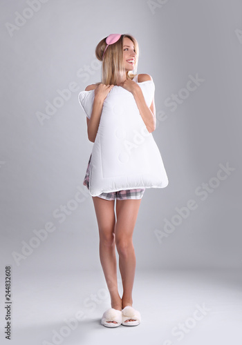 Happy woman in pajamas with pillow on gray background