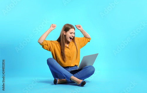 Emotional young woman with laptop celebrating victory on color background © New Africa